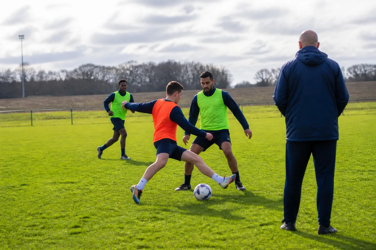 Entraînement de football amateur sur terrain herbeux avec joueurs et éducateurs en pleine séance