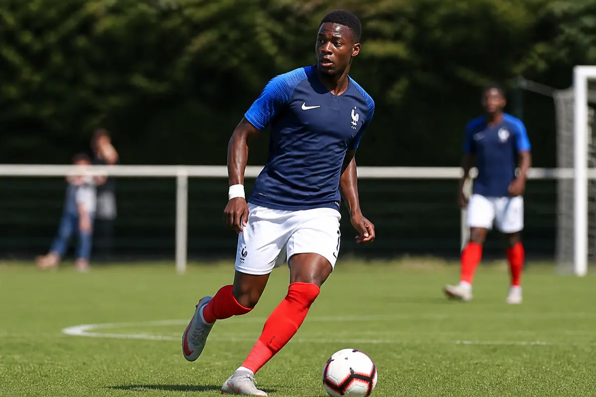Joueur de foot noir en maillot bleu court sur terrain lors d'un match entraînement